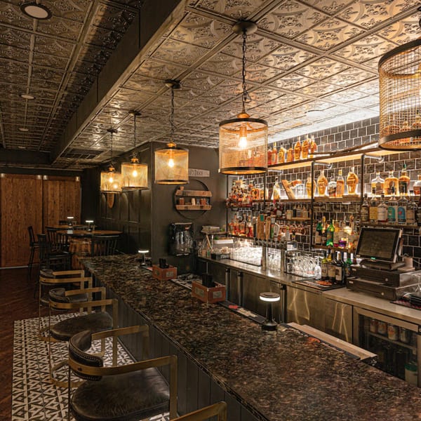 The Barrel Room at Beckett’s bar with a dark granite counter, bar stools, and liquor bottles on shelves.