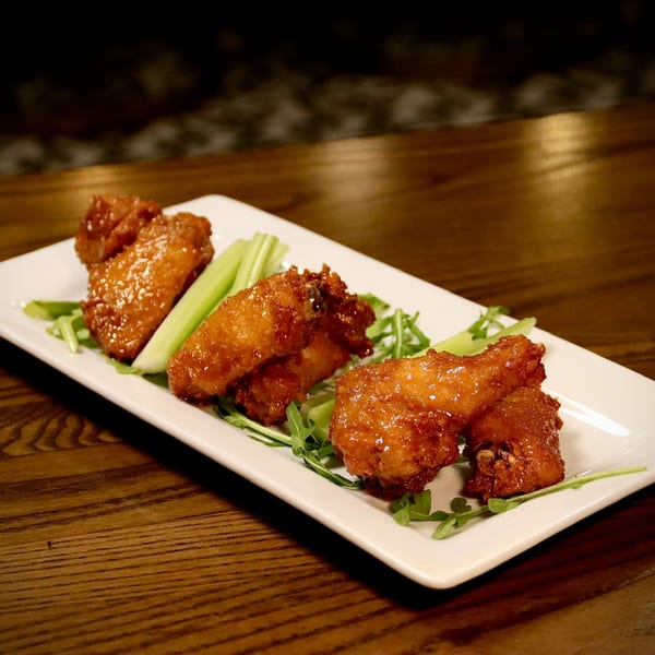 Glazed chicken wings with celery sticks and arugula on a white rectangular plate.