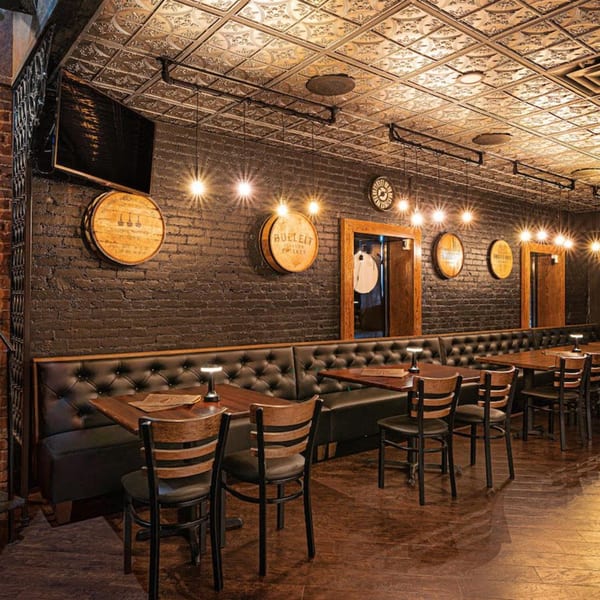 The Barrel Room at Beckett’s features a dark, rustic interior with brick walls, barrel decor, and booth seating.