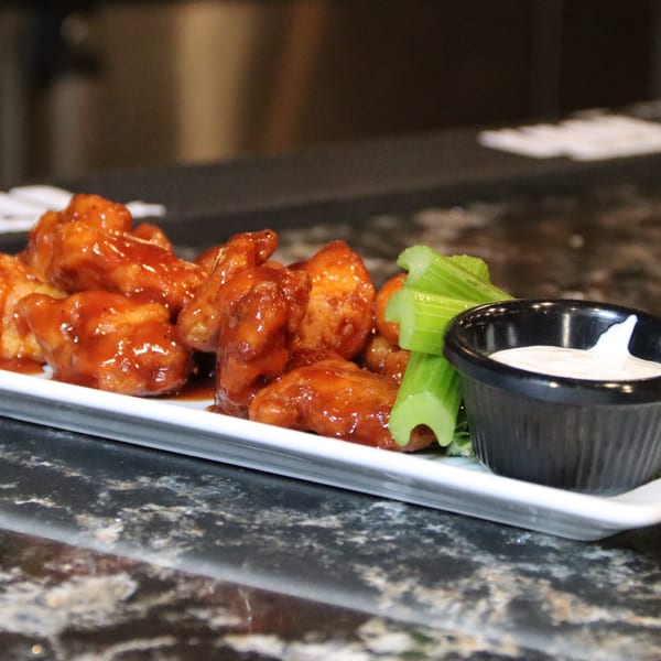 A plate of saucy boneless wings with celery sticks and a side of ranch dressing.