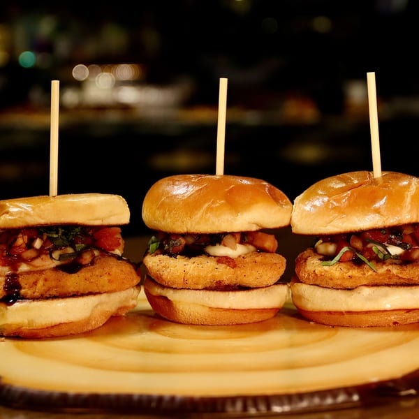 Three American chicken sliders with toppings and toothpicks on a wooden board.