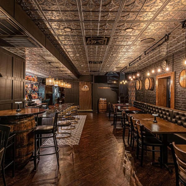 The Barrel Room at Beckett’s features a long bar, dining tables, and a spiral staircase under a tin ceiling.