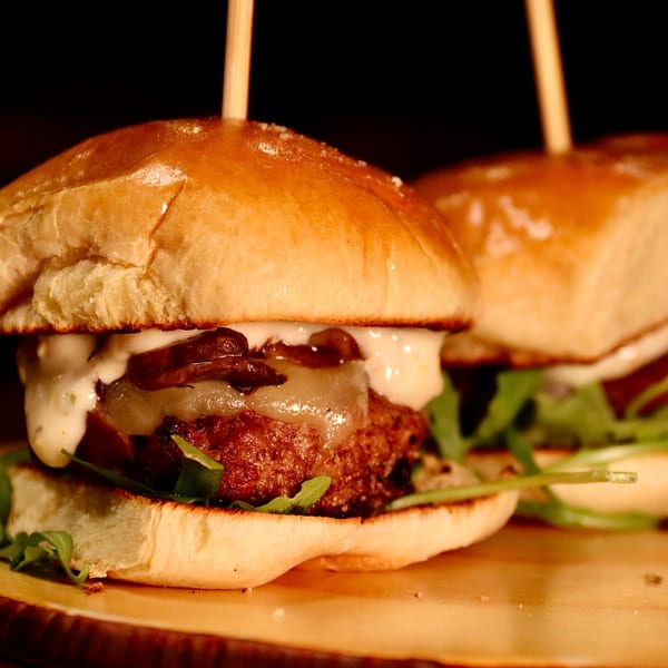 Two gourmet sliders with melted cheese, mushrooms, and arugula on a wooden board.