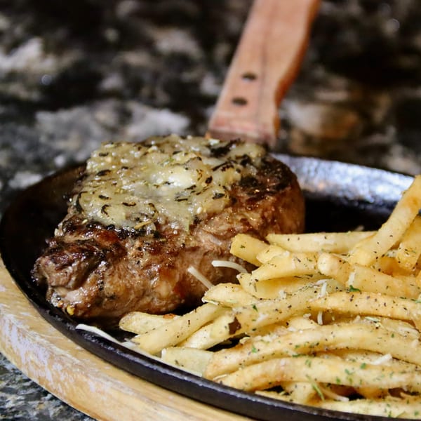 Sizzling steak topped with melted cheese and herbs, served with seasoned french fries on a cast iron skillet.