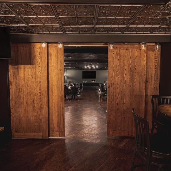 Open wooden barn doors reveal a private dining room with tables, chairs, and a large screen.